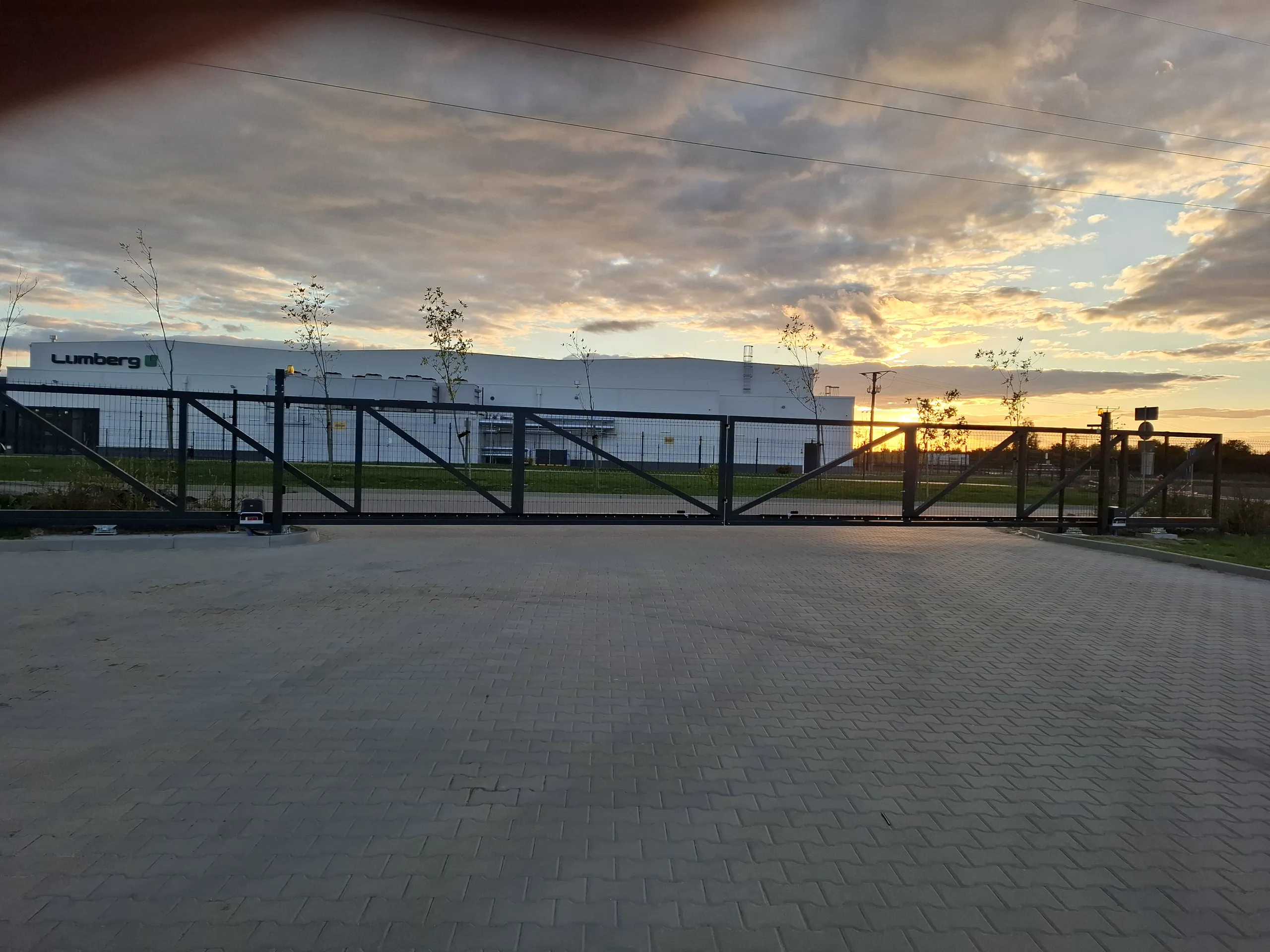Przesuwna brama wjazdowa z paneli stalowych z napędem na utwardzonym podjeździe o zachodzie słońca