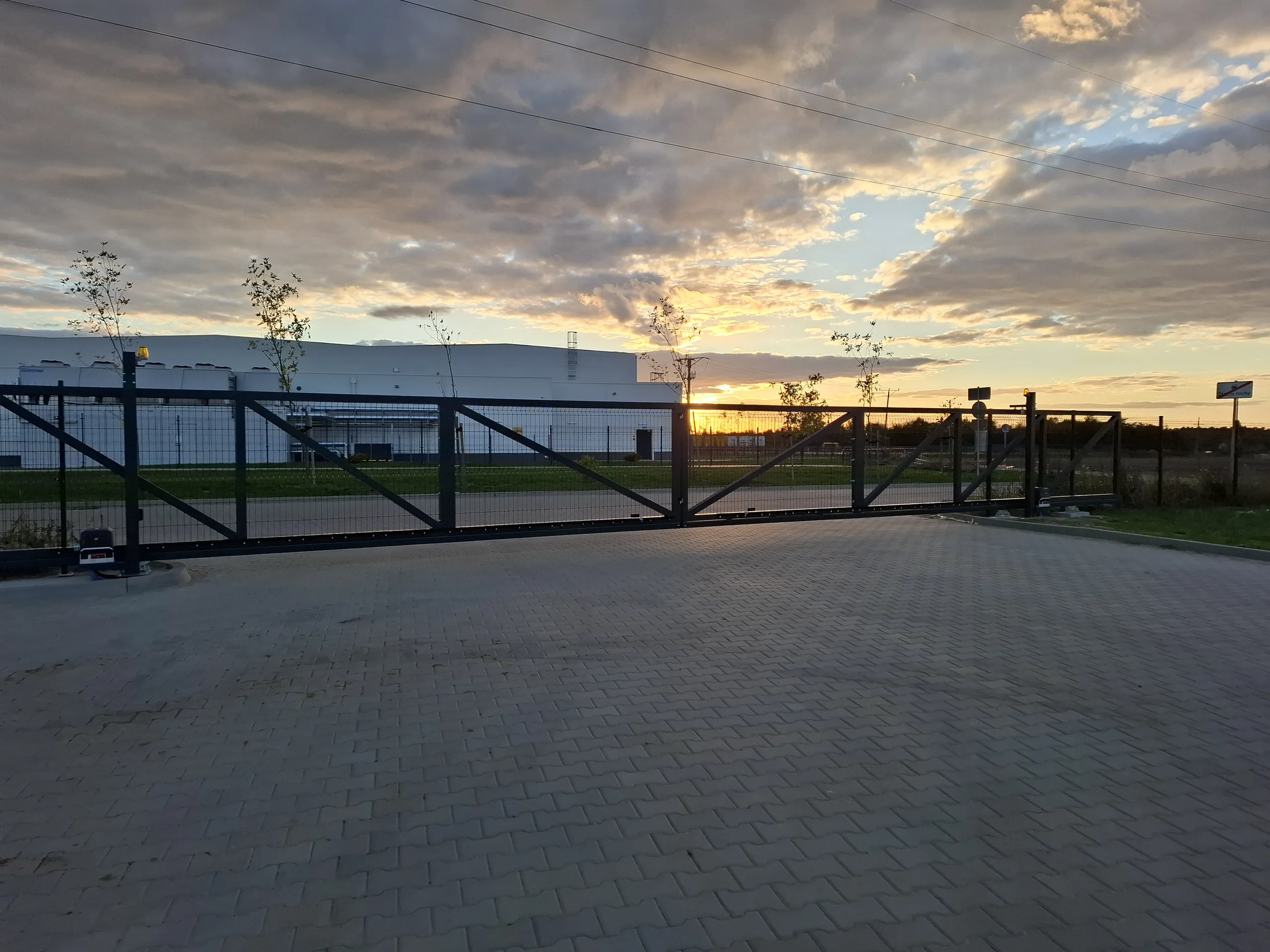 Bramy wjazdowe przesuwne na betonowym podjeździe z metalowymi przęsłami o zachodzie słońca