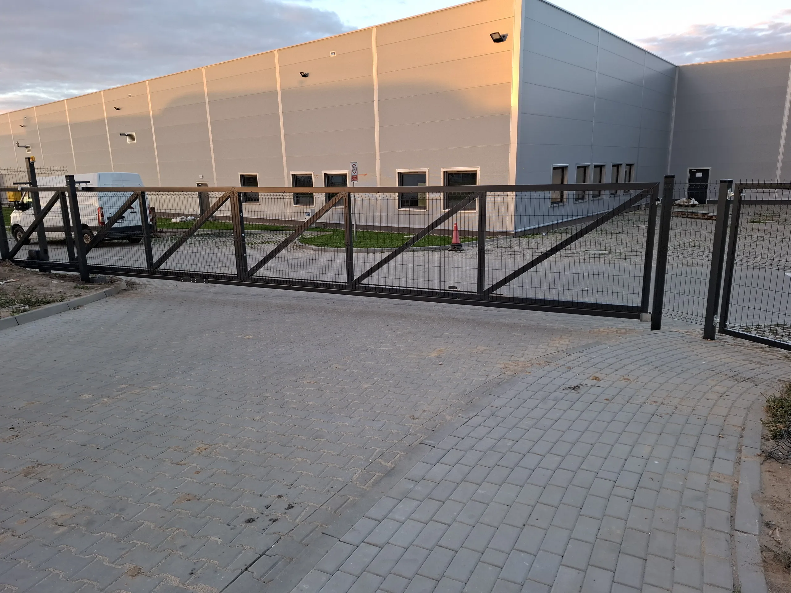 Metalowa brama wjazdowa panelowa na prowadnicach przed budynkiem przemysłowym
