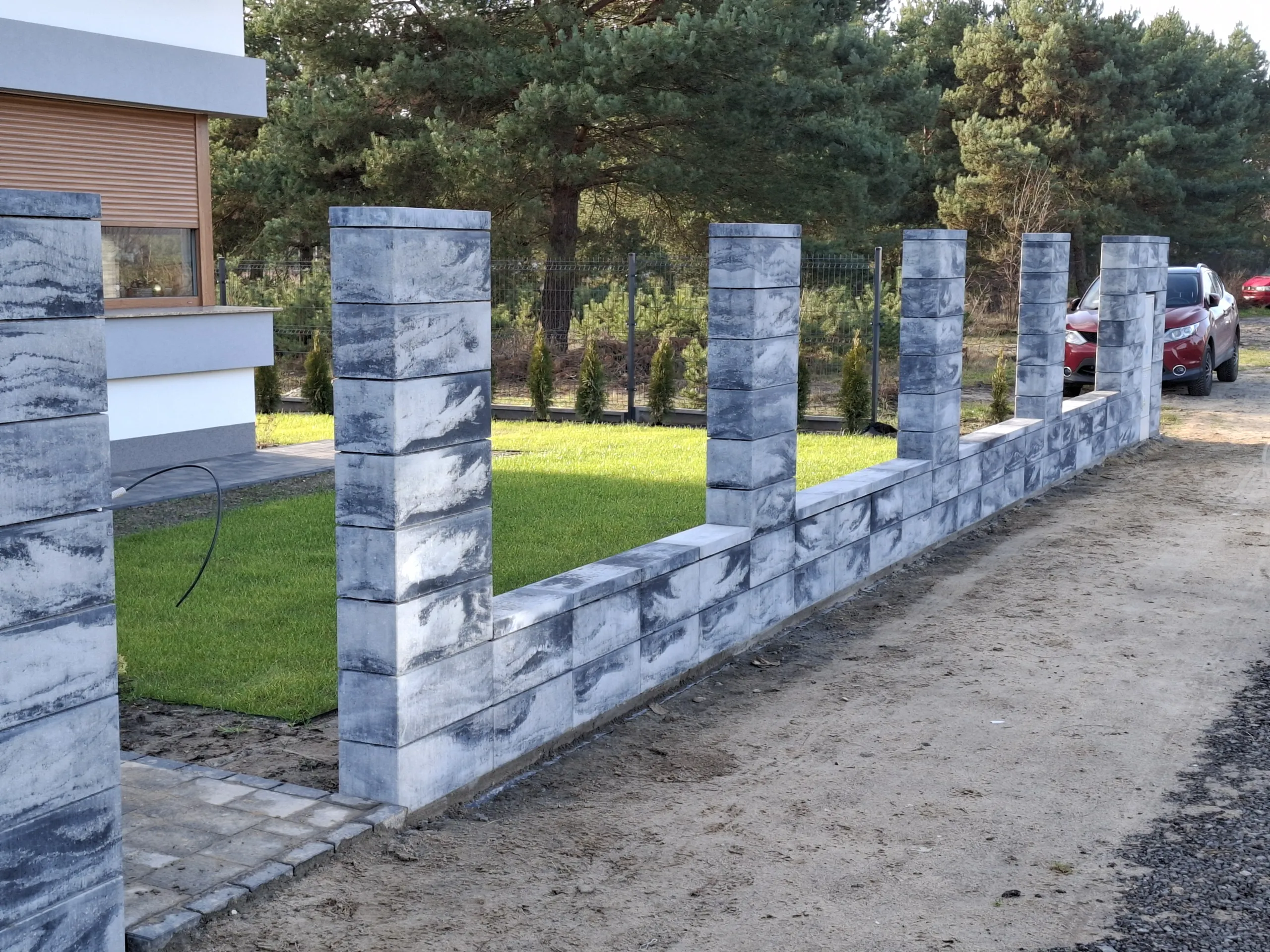 Nowoczesne ogrodzenie z bloczków betonowych: masywne słupki i łącząca je niska ścianka