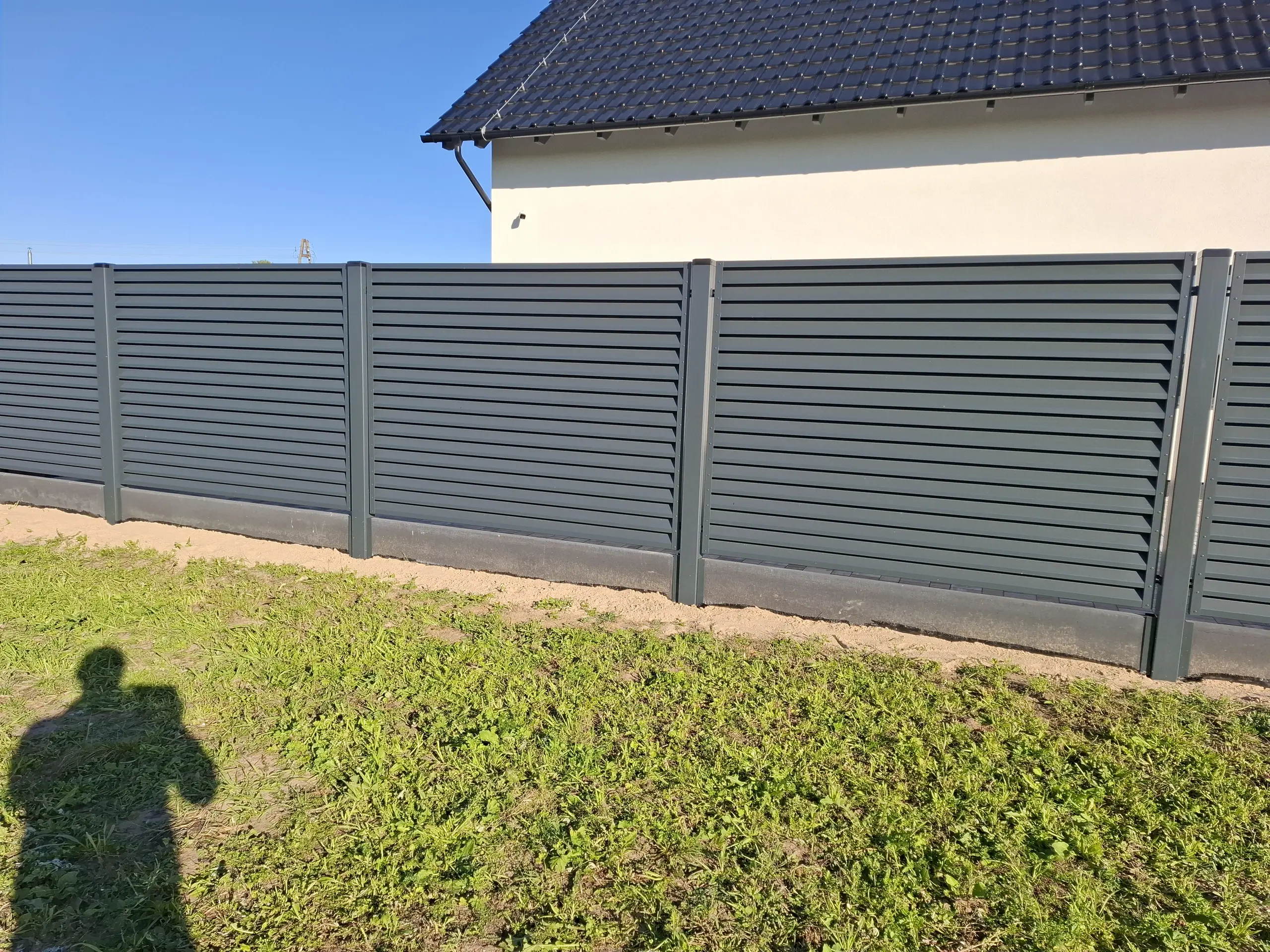 Ogrodzenie żaluzjowe w nowoczesnym stylu – ciemnoszare poziome panele na tle trawnika i fragmentu posesji