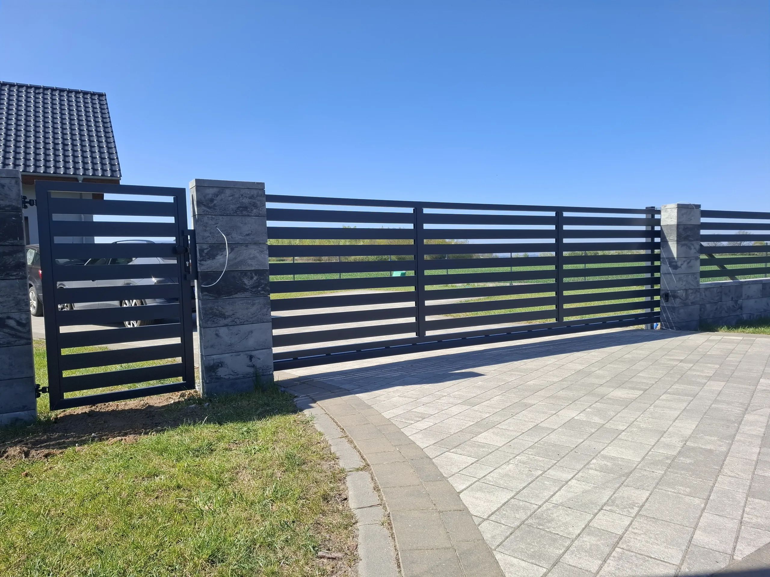 Nowoczesne ogrodzenie żaluzjowe na betonowych słupach z furtką i przesuwną bramą wjazdową