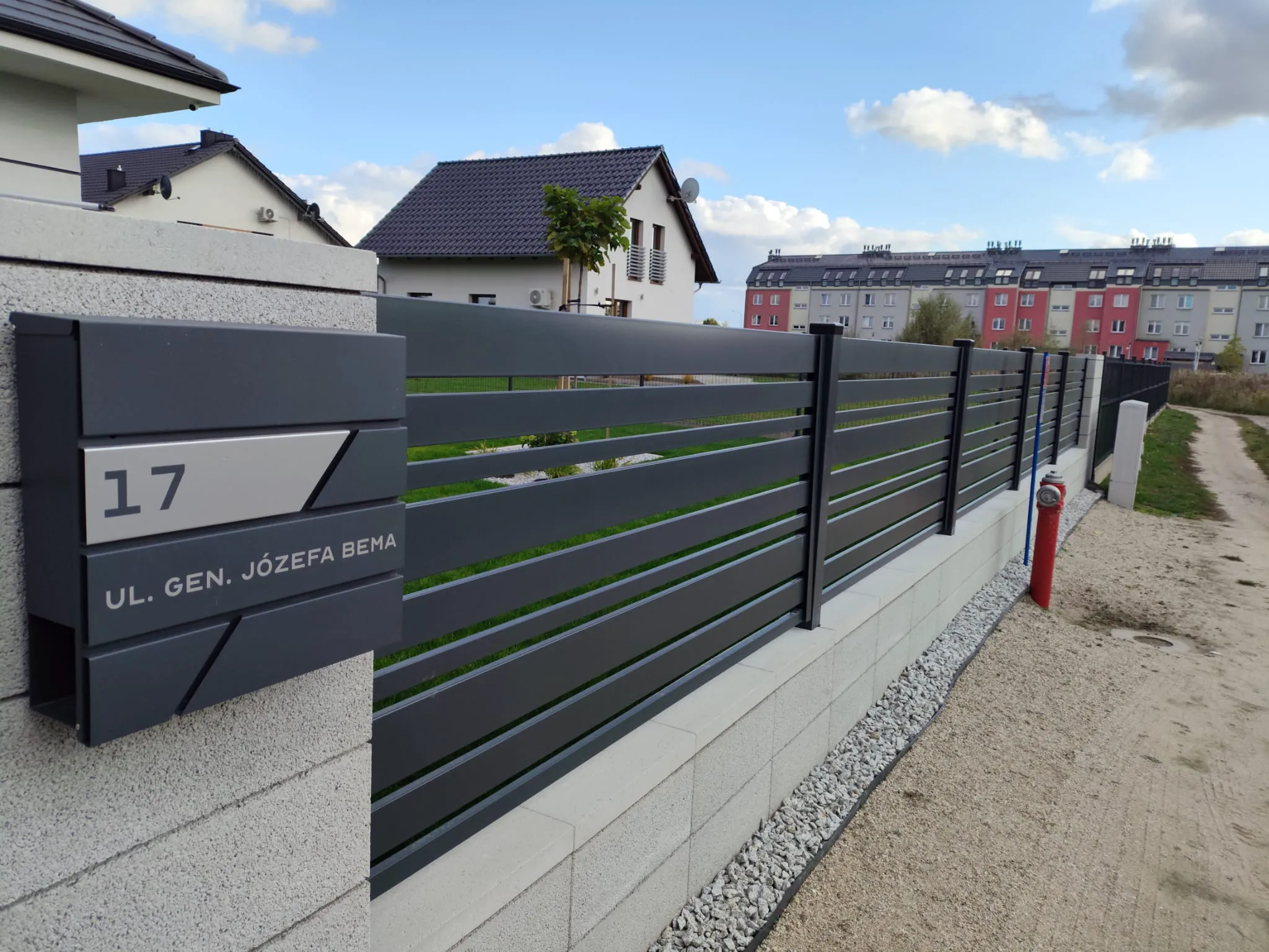 Ogrodzenie żaluzjowe z metalowych poziomych przęseł osadzone na betonowej podmurówce przed domem